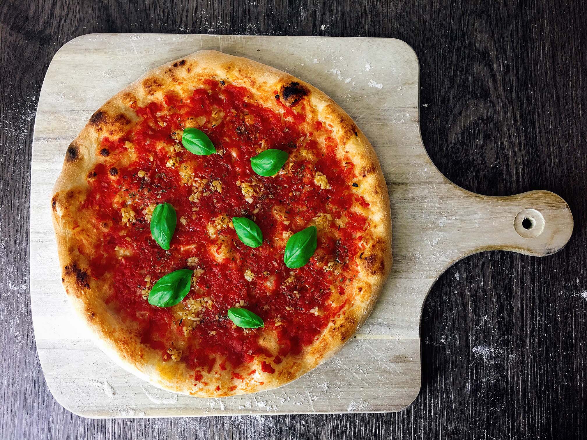 une belle pizza Marinara avec sa sauce tomate, ses feuilles de basilic et son ail doré au four, posée sur une planche en bois